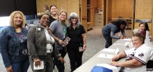 portrait group of five women plus two others at a check-in table